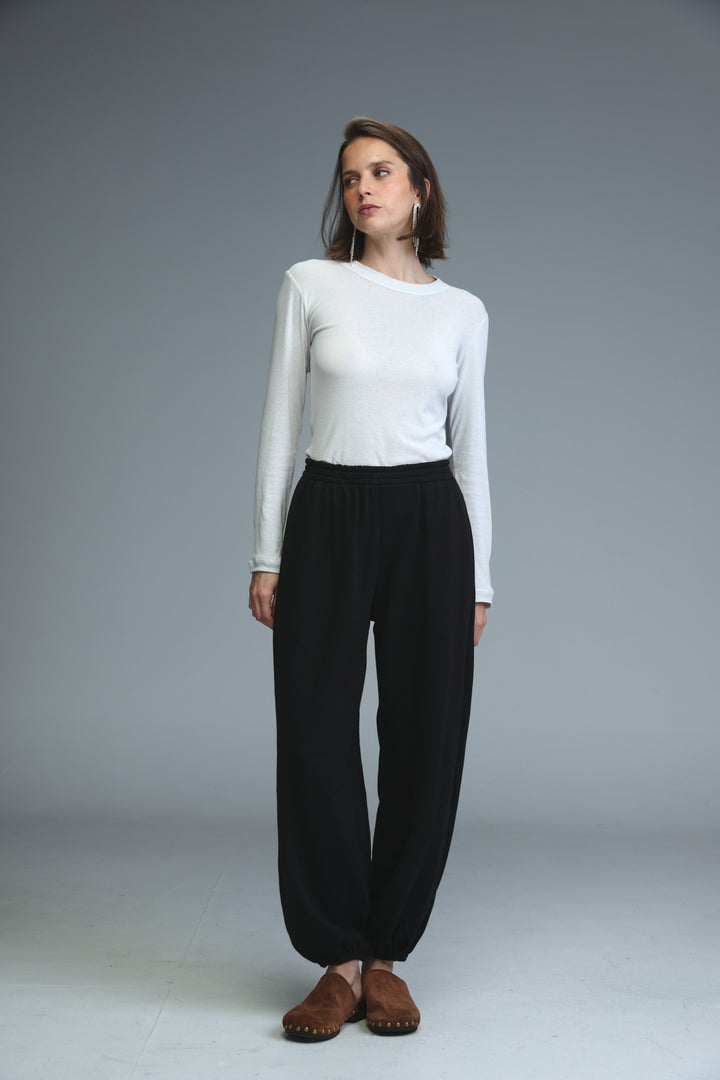 A woman wears black high-waisted wide-leg joggers paired with a white long-sleeved top and brown moccasins