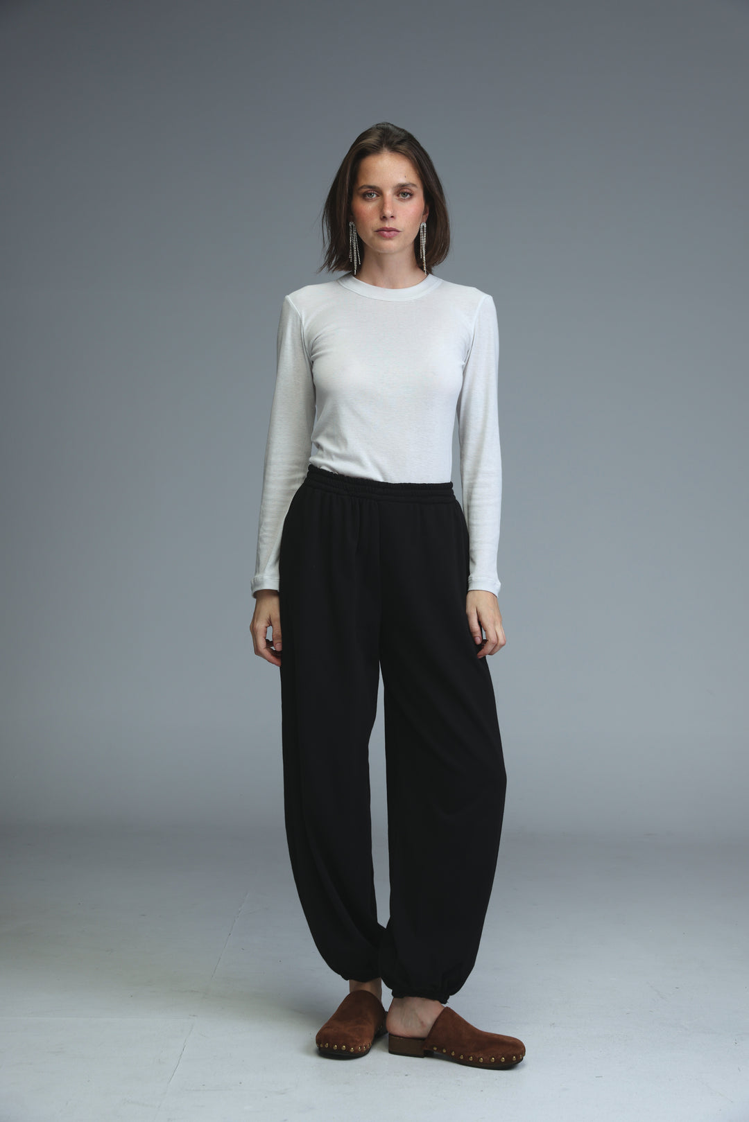 A woman wearing black joggers paired with a white long-sleeved top and brown moccasin-style shoes