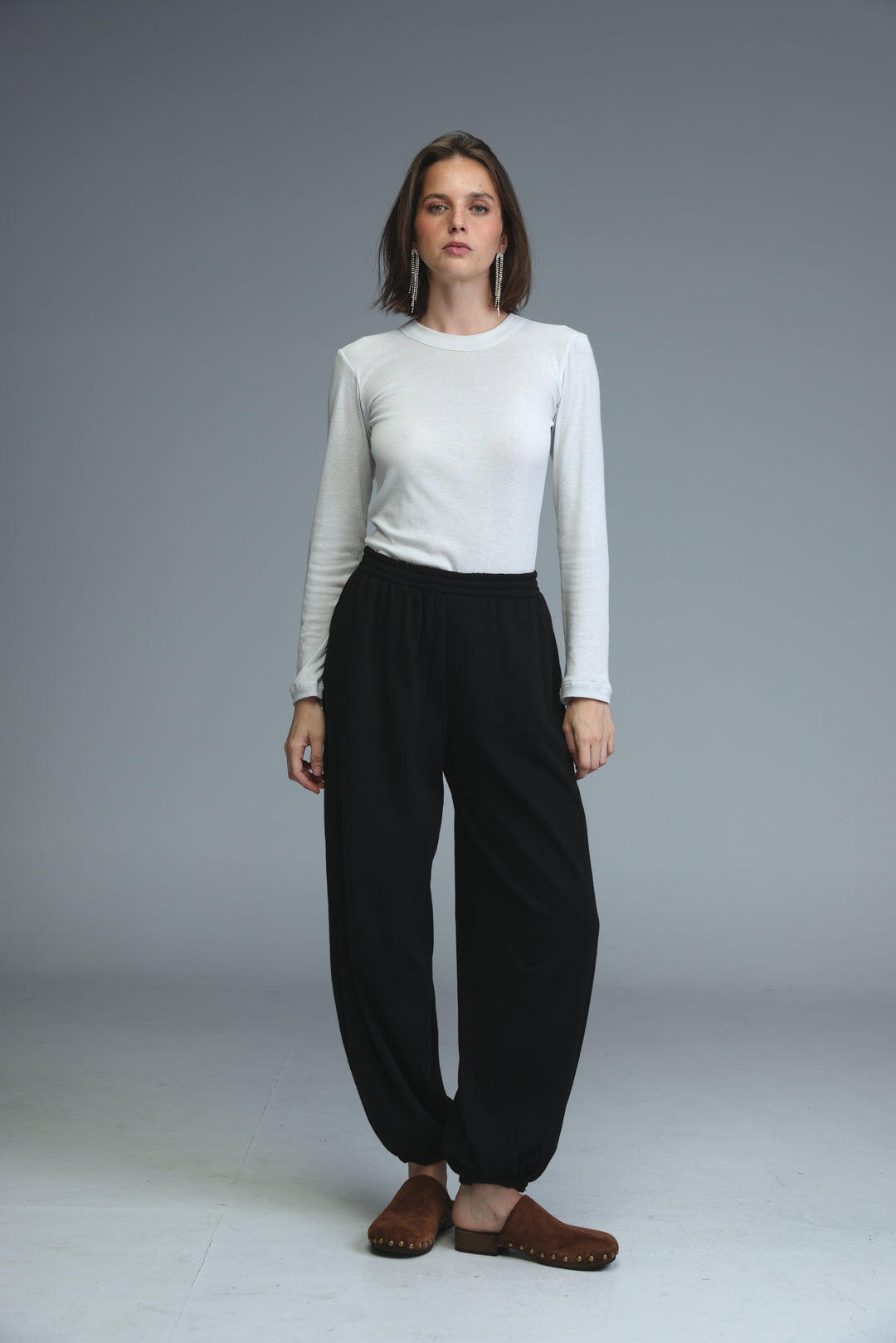 A woman wearing black high-waisted wide-leg joggers paired with a white long-sleeved top and brown wooden clogs