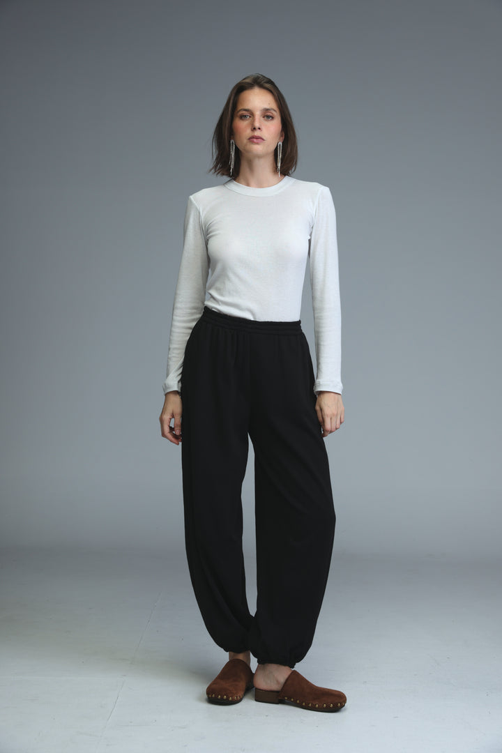 A woman wearing black high-waisted wide-leg joggers paired with a white long-sleeved top and brown wooden clogs