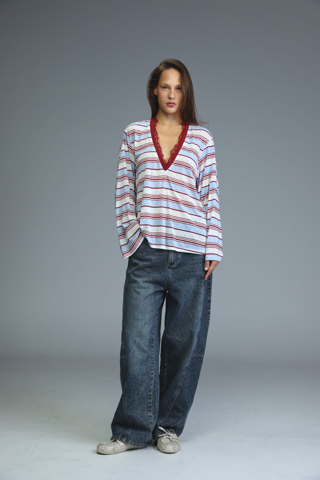 A woman wears a front view long-sleeved glow red striped shirt with white, light blue, and red stripes and red lace trim