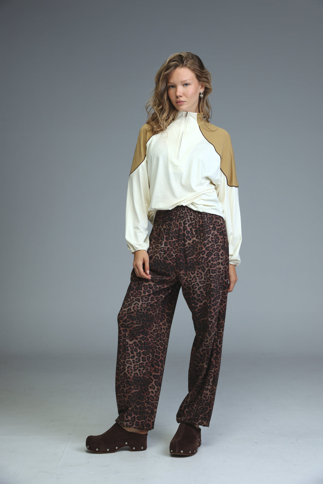 A woman wearing front view brown leopard joggers paired with a two-tone white and beige long-sleeved top