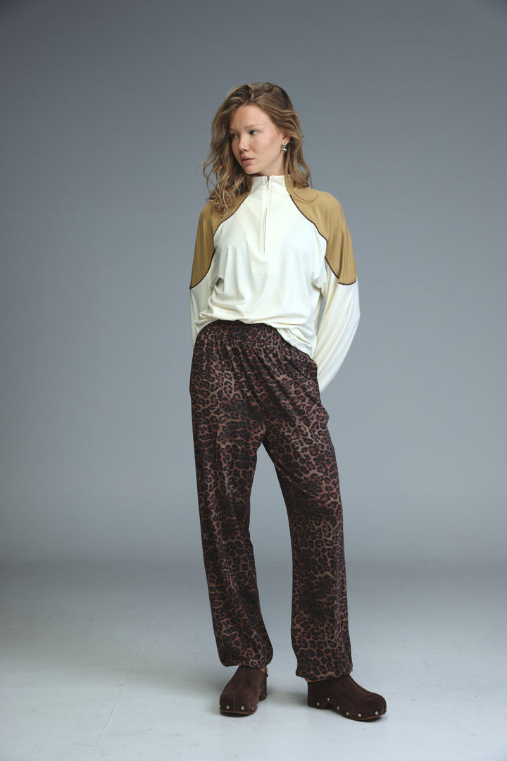 A woman wearing dark brown leopard joggers paired with a beige and white two-tone long-sleeved top from the front