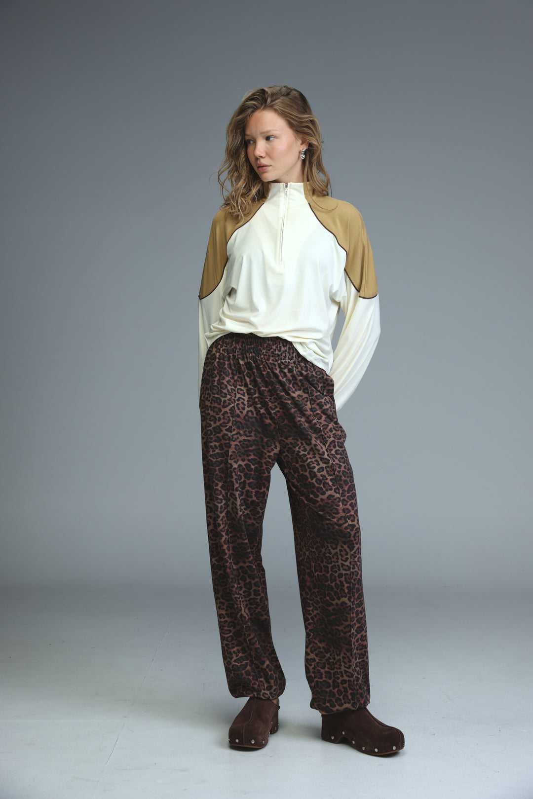 A front view of best leopard joggers in dark brown with black spots paired with a beige and white two-tone zip-up top