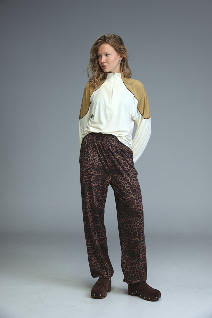 A front view of best leopard joggers in dark brown with black spots paired with a beige and white two-tone zip-up top