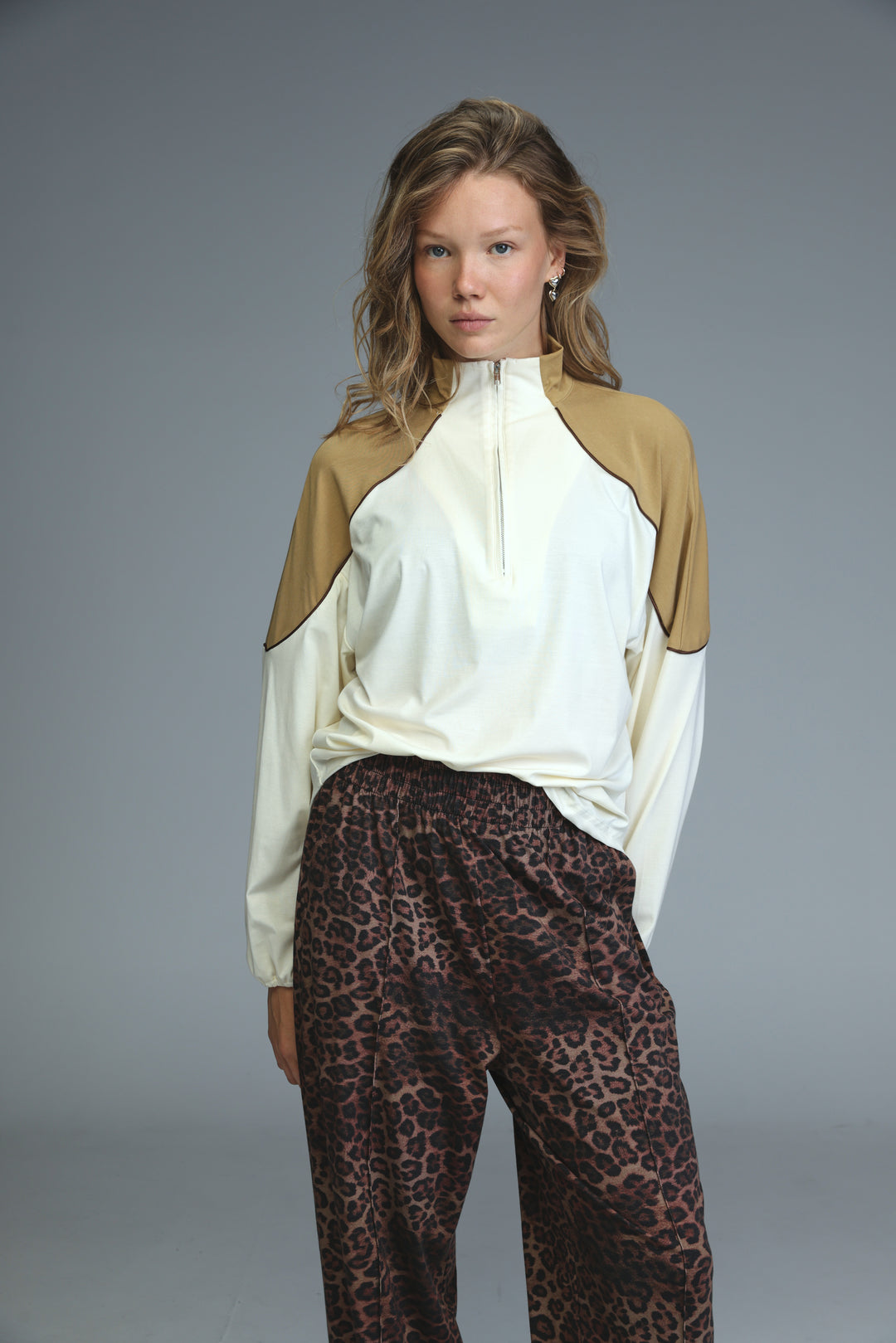 A woman wearing an allure cream sweatshirt with tan color blocks and a front zip up with long sleeves