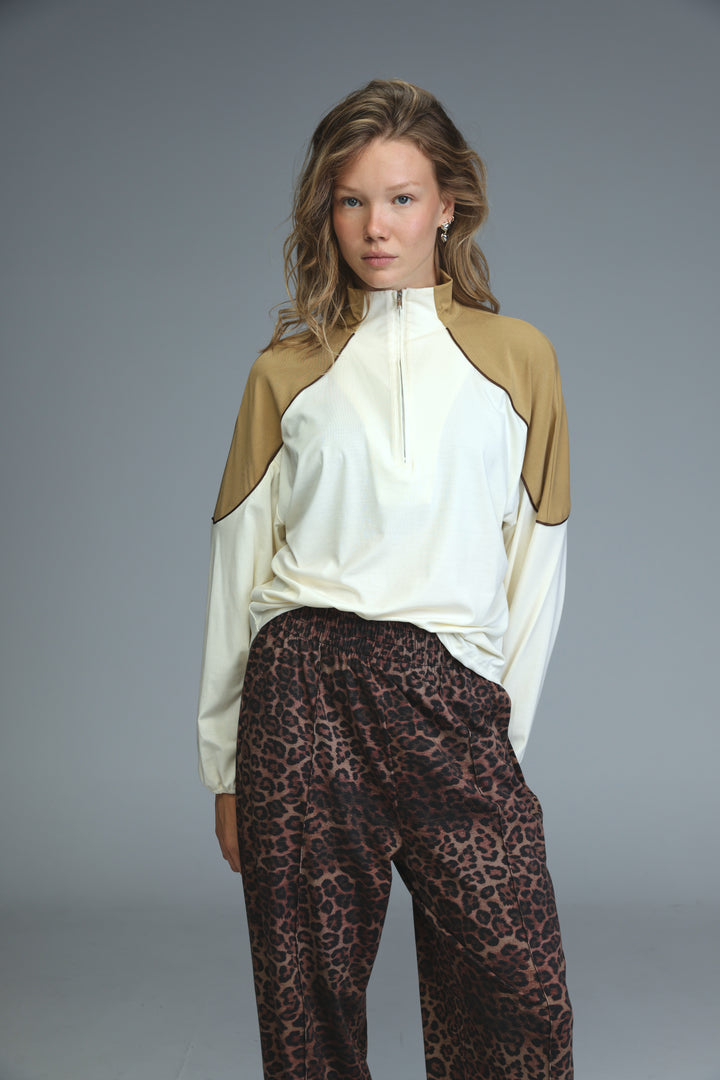 A woman wearing an allure cream sweatshirt with tan color blocks and a front zip up with long sleeves