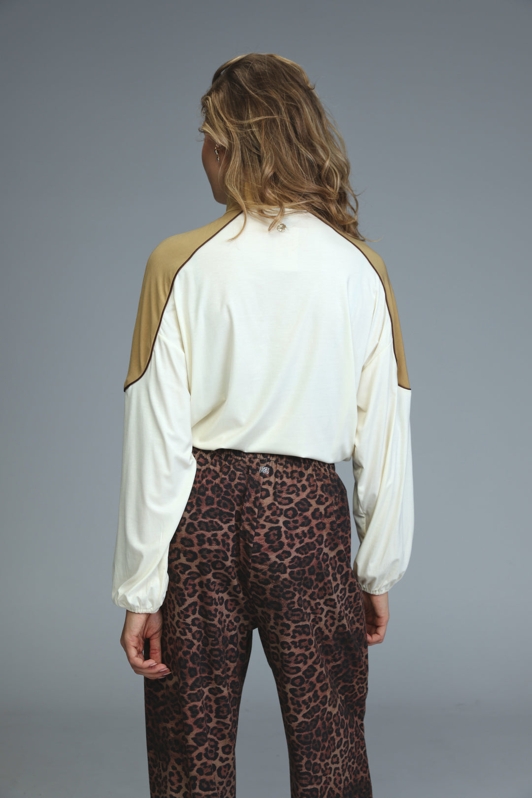 A woman wears a front view allure cream sweatshirt with tan raglan sleeves paired with leopard-print pants