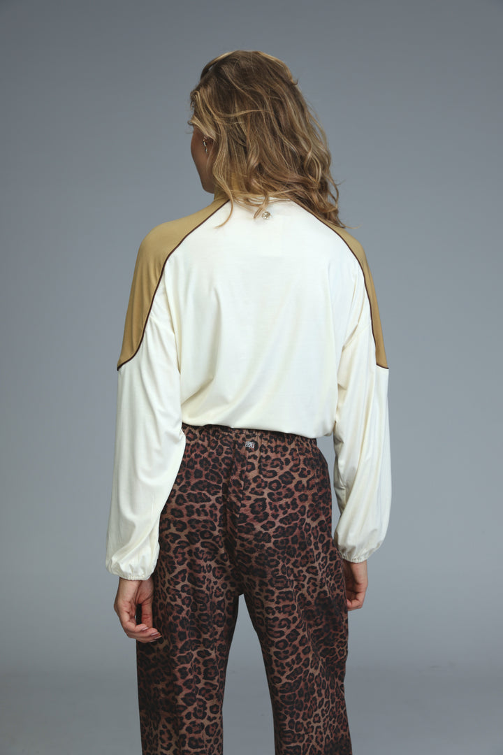 A woman wears a front view allure cream sweatshirt with tan raglan sleeves paired with leopard-print pants