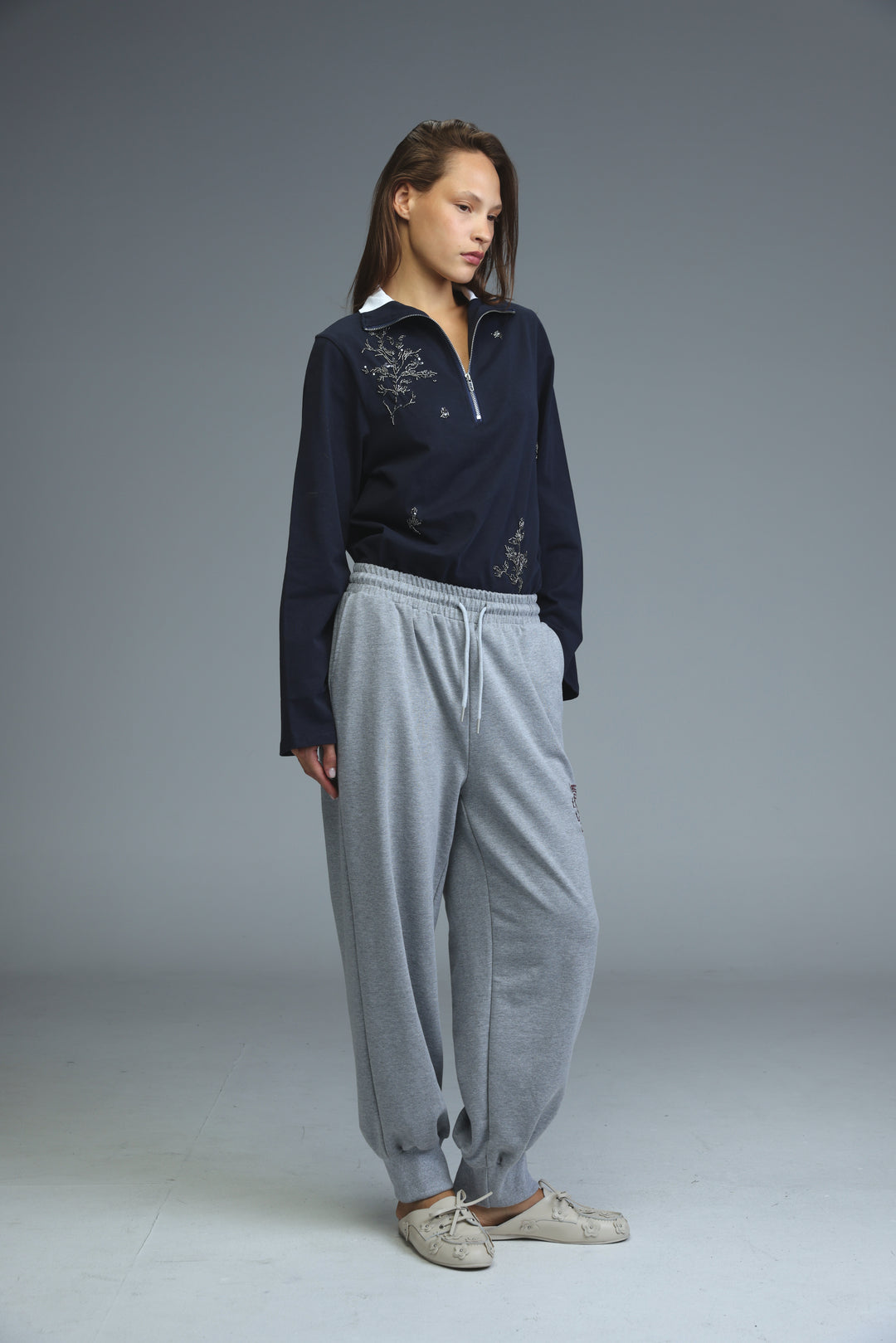 Navy blue long-sleeved top with delicate silver embroidery and half-zip collar shown from the front with grey joggers