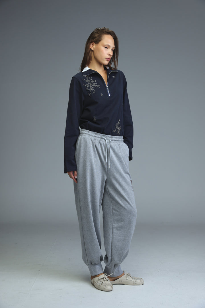 Navy blue long-sleeved top with delicate silver embroidery and half-zip collar shown from the front with grey joggers