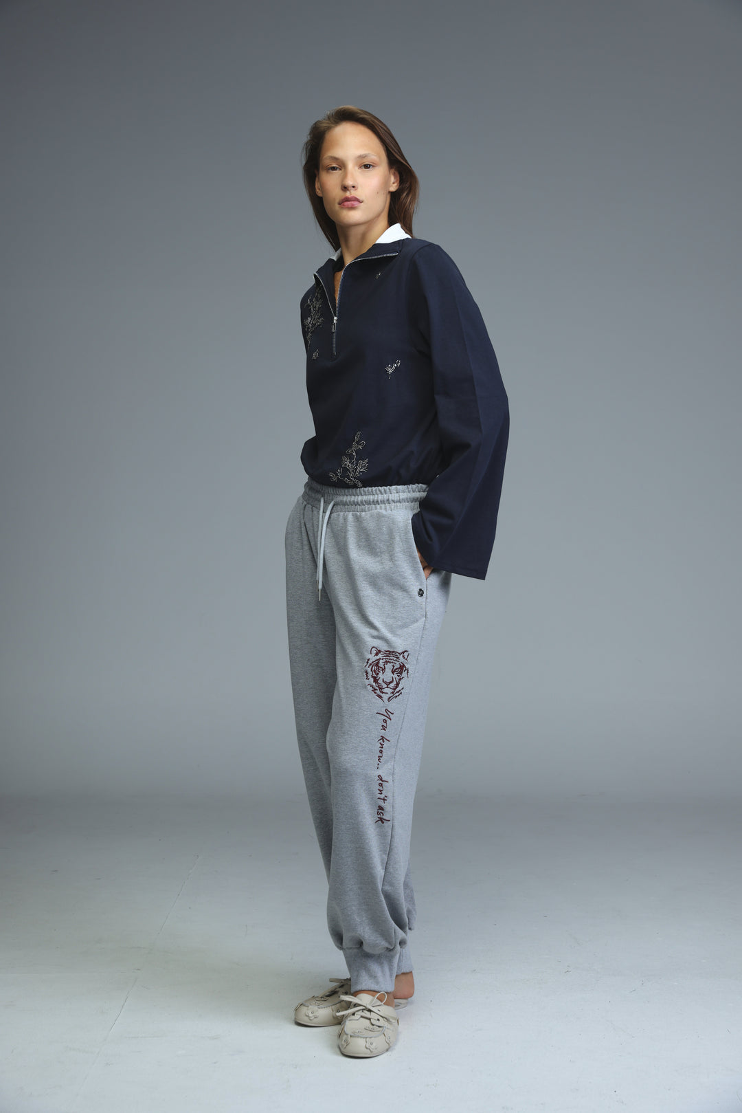 Navy blue zip-up jacket with white collar and subtle embroidered details shown from the front with iconic grey joggers