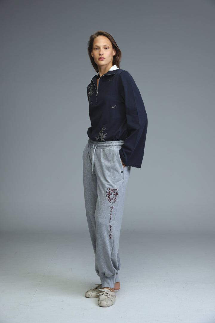 Navy blue zip-up jacket with white collar and subtle embroidered details shown from the front with iconic grey joggers
