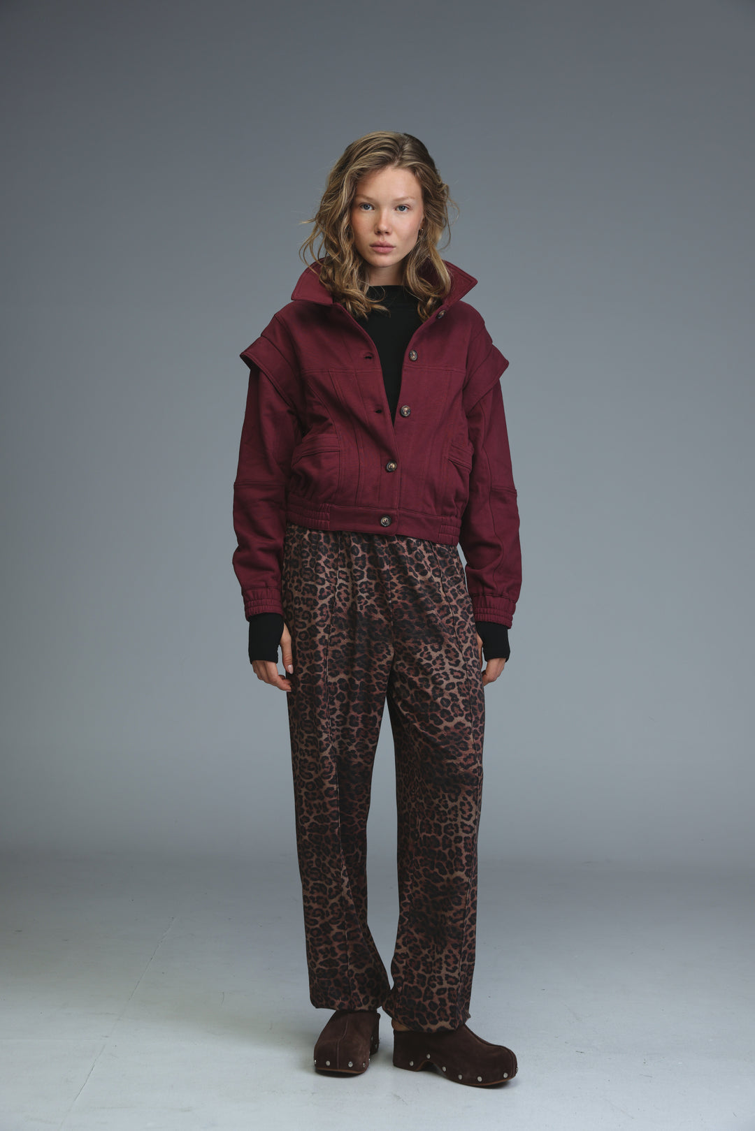 Maroon cropped hooded jacket with button closure worn over black gloves front view