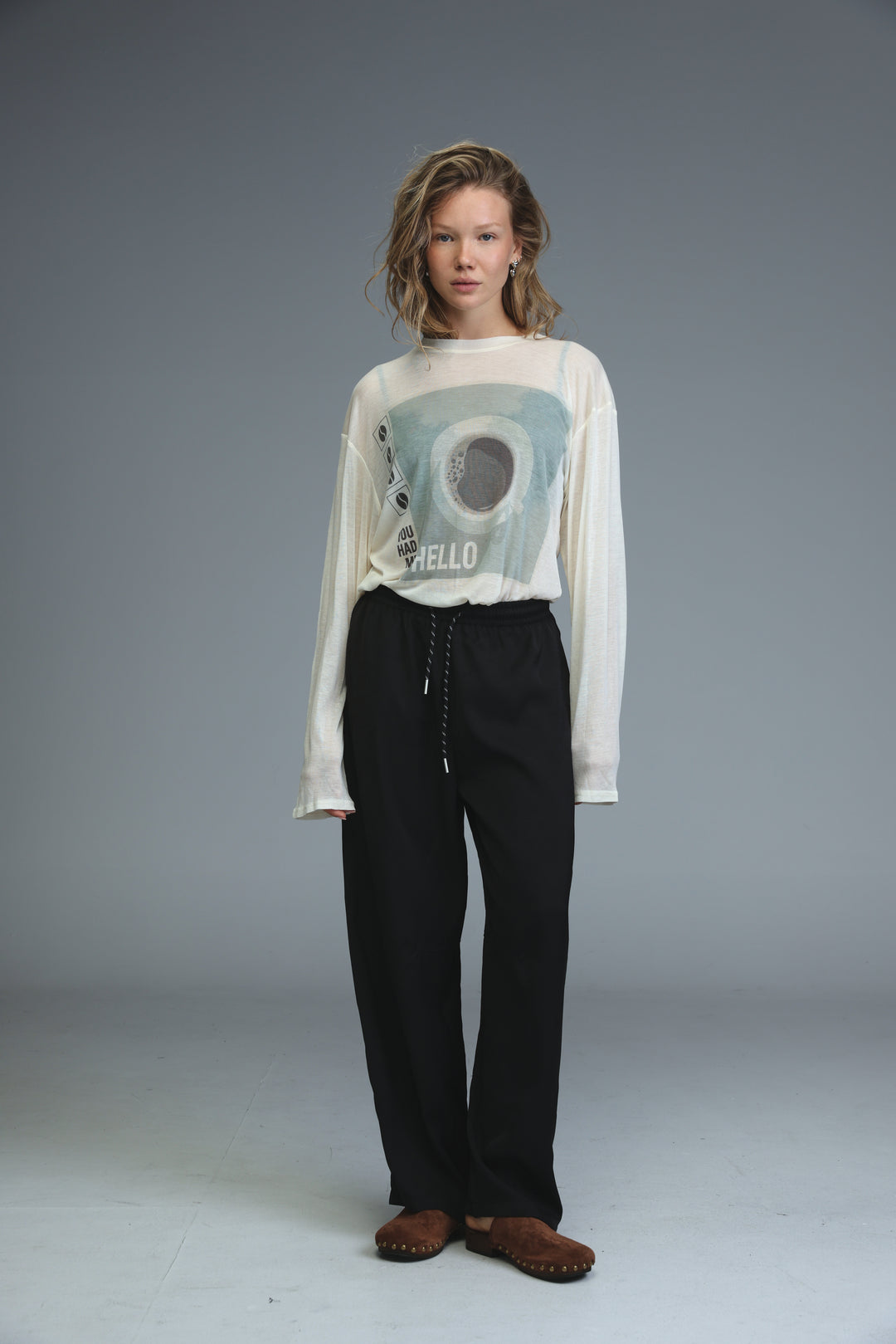 White long-sleeved graphic tee with circular black hello design paired with golden black bottoms shown from front