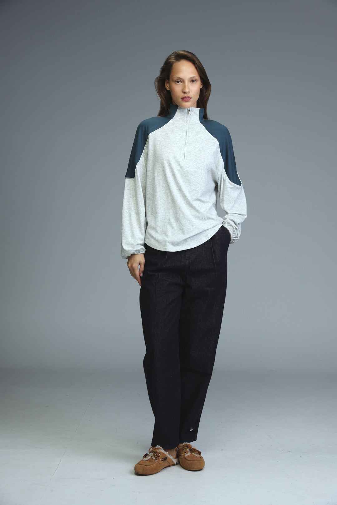 A grey sweatshirt with long sleeves shown front view worn with a white and navy blue half-zip jacket and black trousers