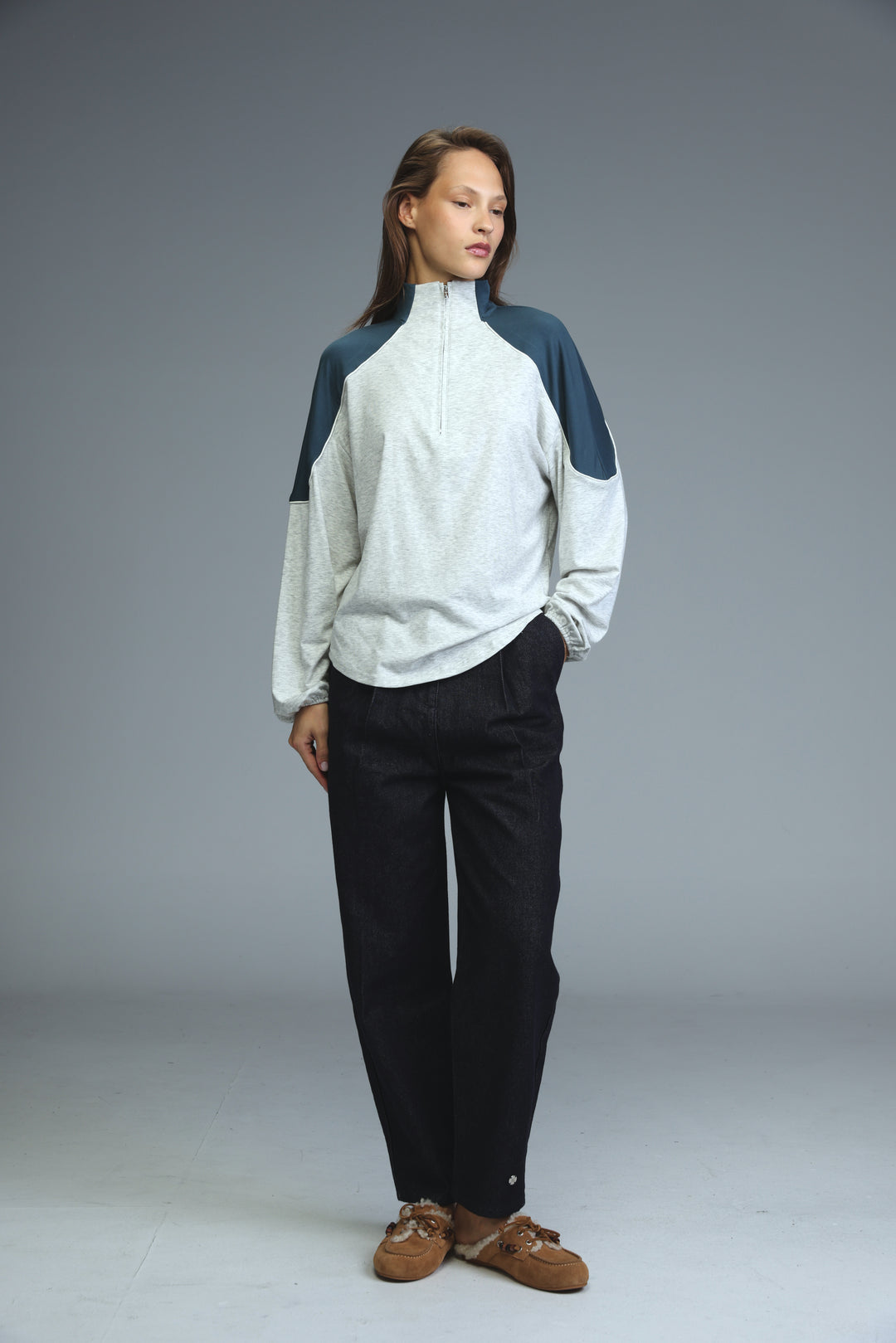 A woman wearing an allure grey sweatshirt with navy color blocking and a half-zip front paired with black trousers