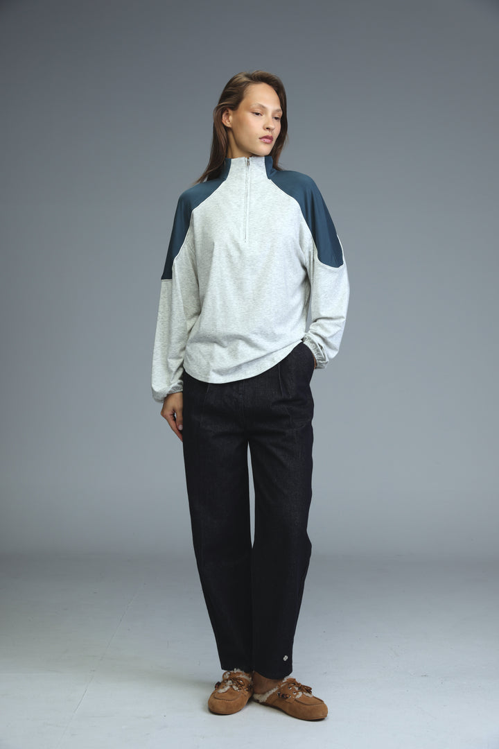A woman wearing an allure grey sweatshirt with navy color blocking and a half-zip front paired with black trousers