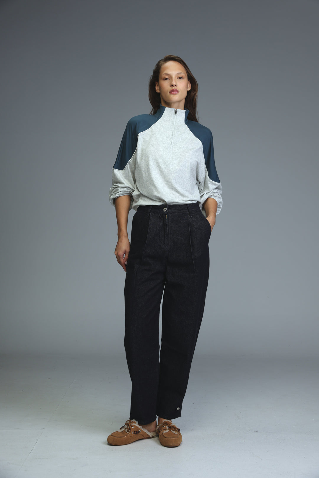 A front view of dark blue tailored denim trousers paired with a white and navy blue color-blocked zip-up top with rolled sleeves