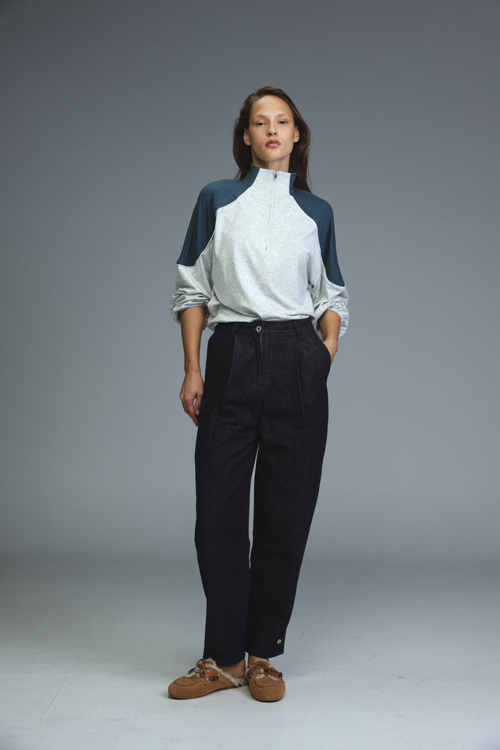 A front view of dark blue tailored denim trousers paired with a white and navy blue color-blocked zip-up top with rolled sleeves