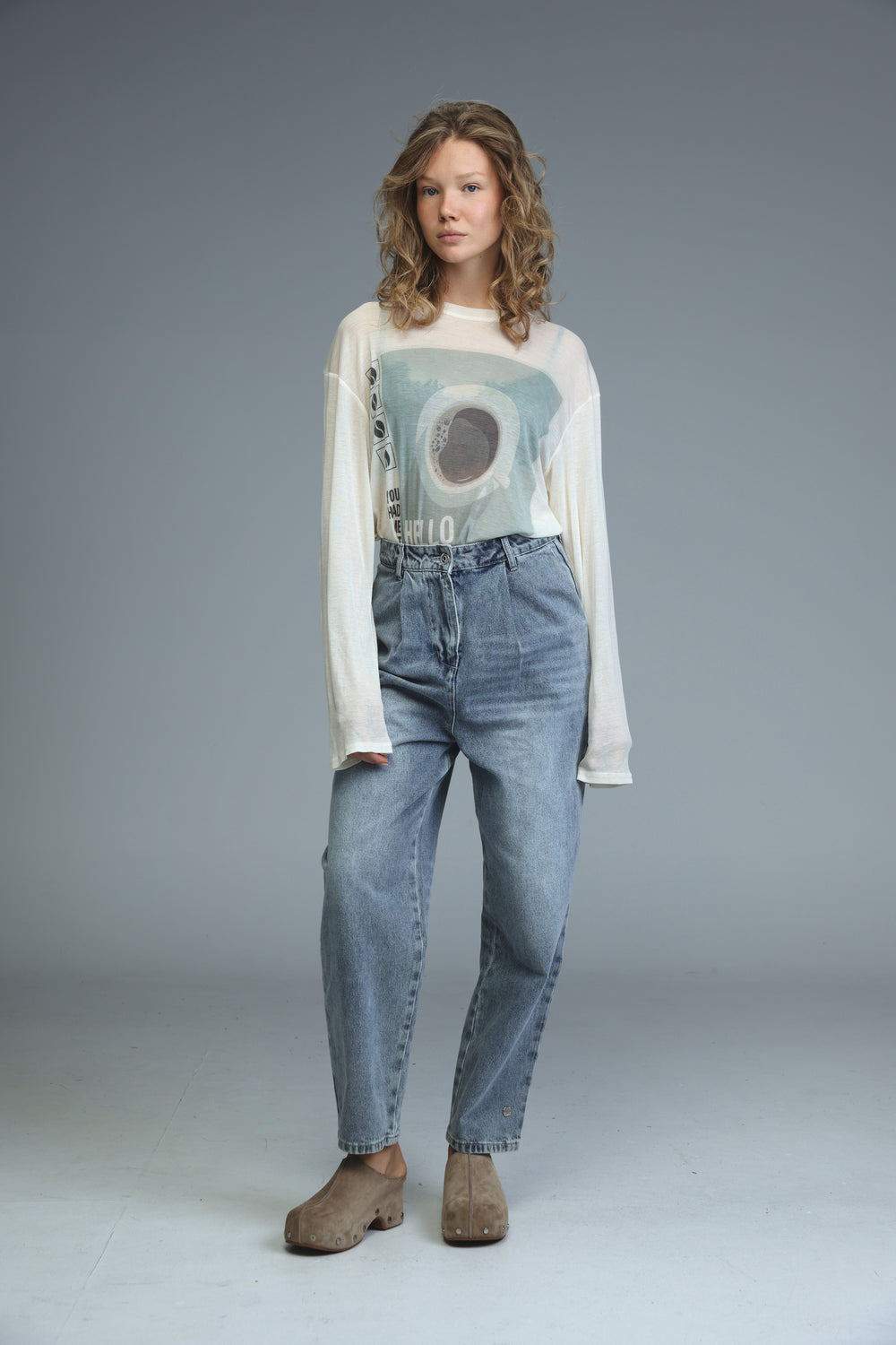 Woman wearing hello coffee cream long-sleeved shirt with light blue graphic print and high-waisted medium-wash jeans front view