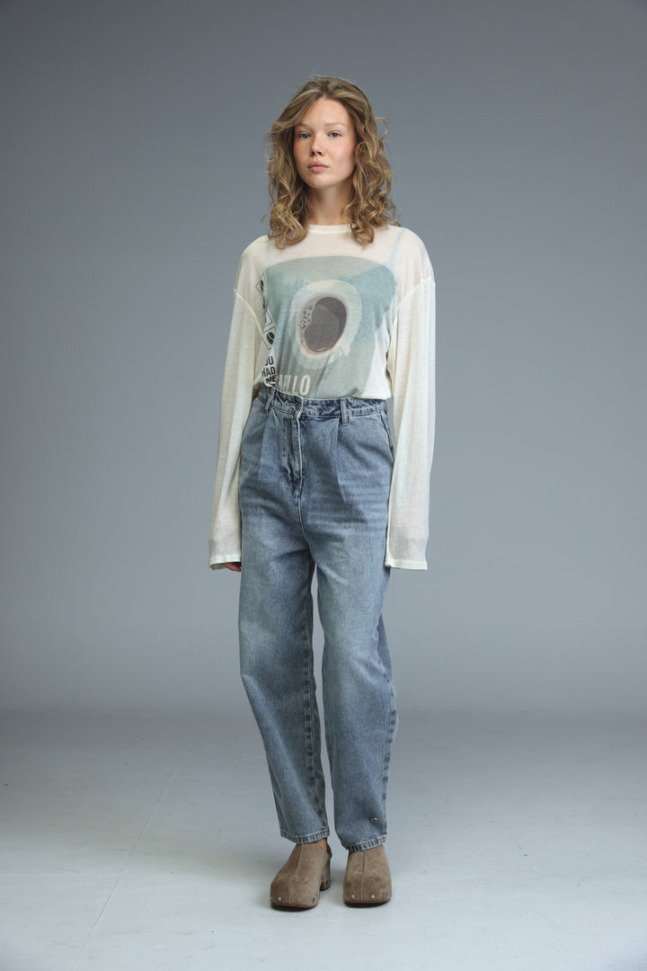 A woman wears a hello coffee cream shirt with light blue and gray graphic print over high-waisted denim jeans front view