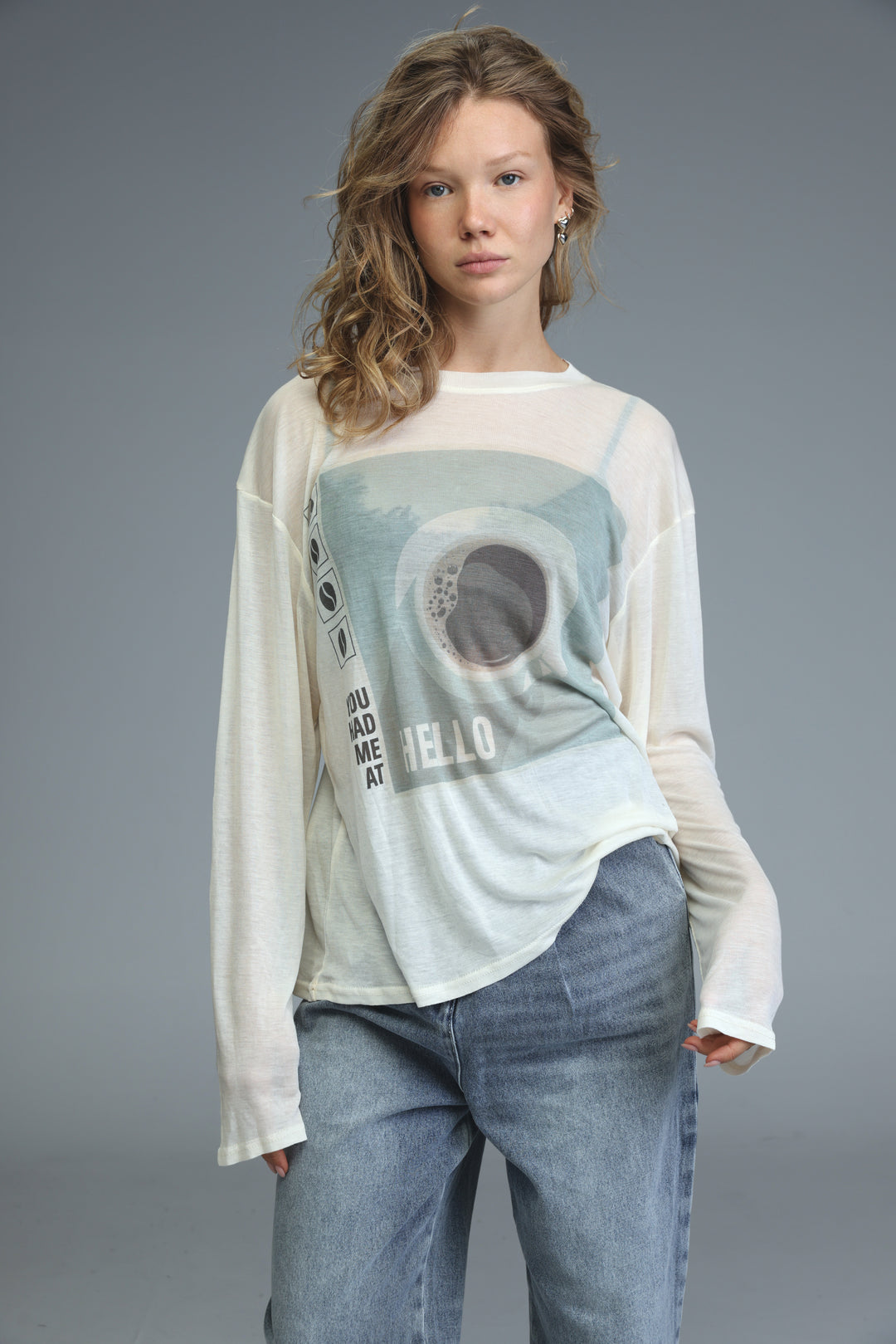 White long-sleeved Hello Coffee Cream shirt with a faded blue and gray eye design and text you mad me at hello on front