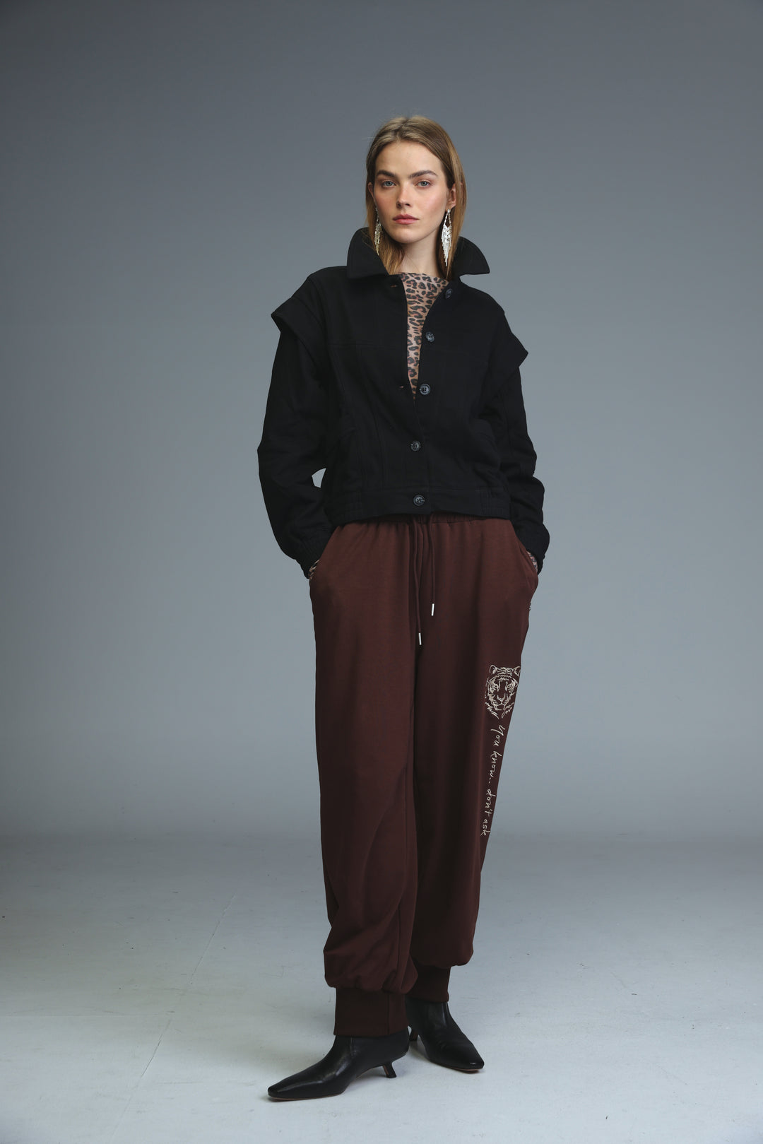 A woman wears iconic brown joggers with an embroidered tiger design on the side seam paired with a black jacket