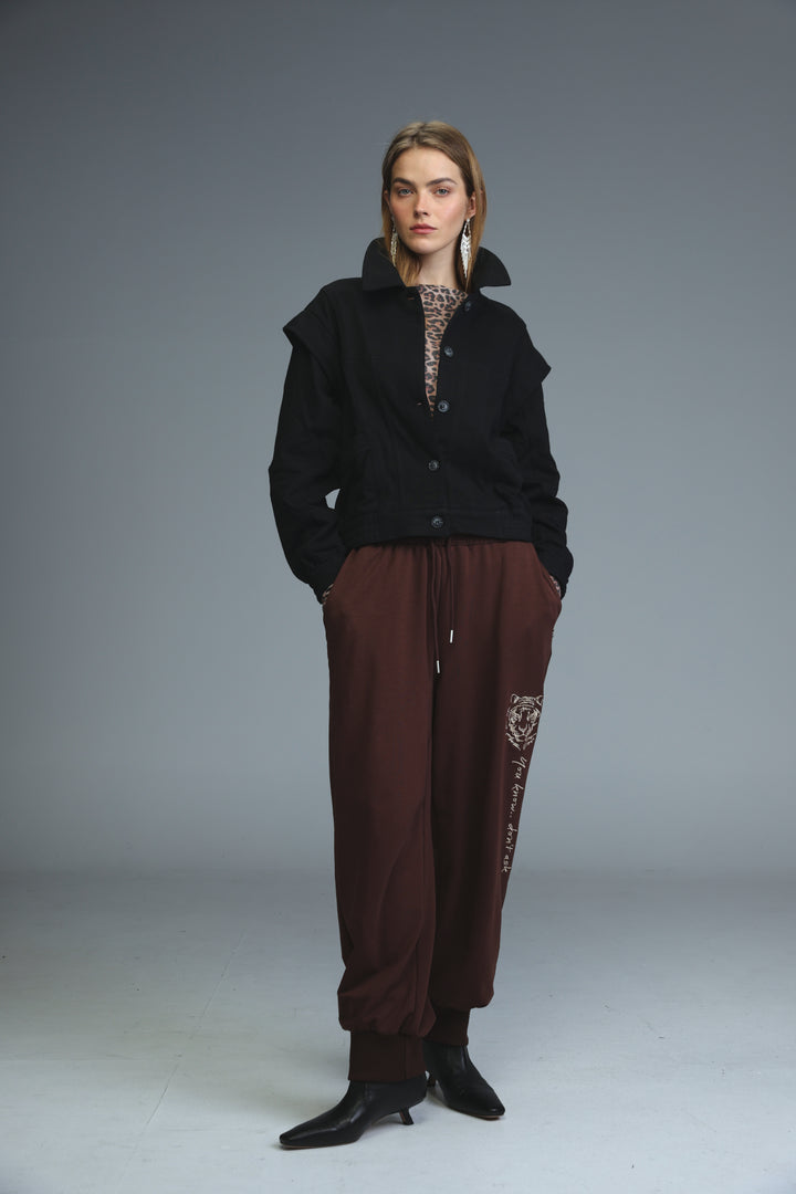 A woman wears iconic brown joggers with an embroidered tiger design on the side seam paired with a black jacket