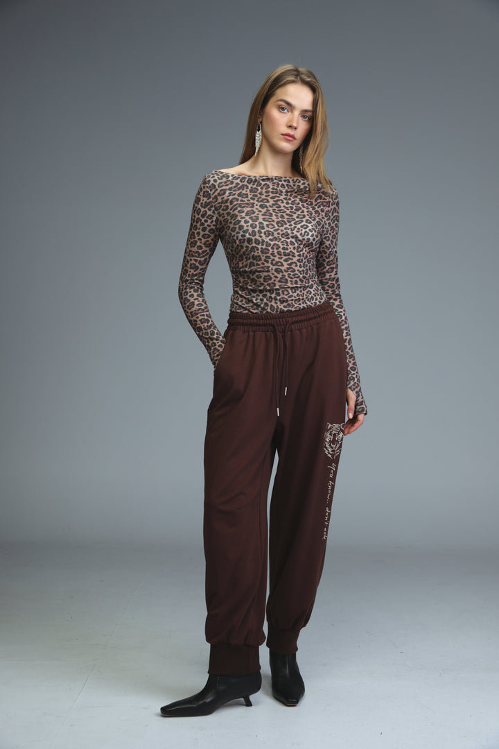 A woman wears iconic brown joggers with embroidered side detailing paired with a leopard-print long-sleeved top