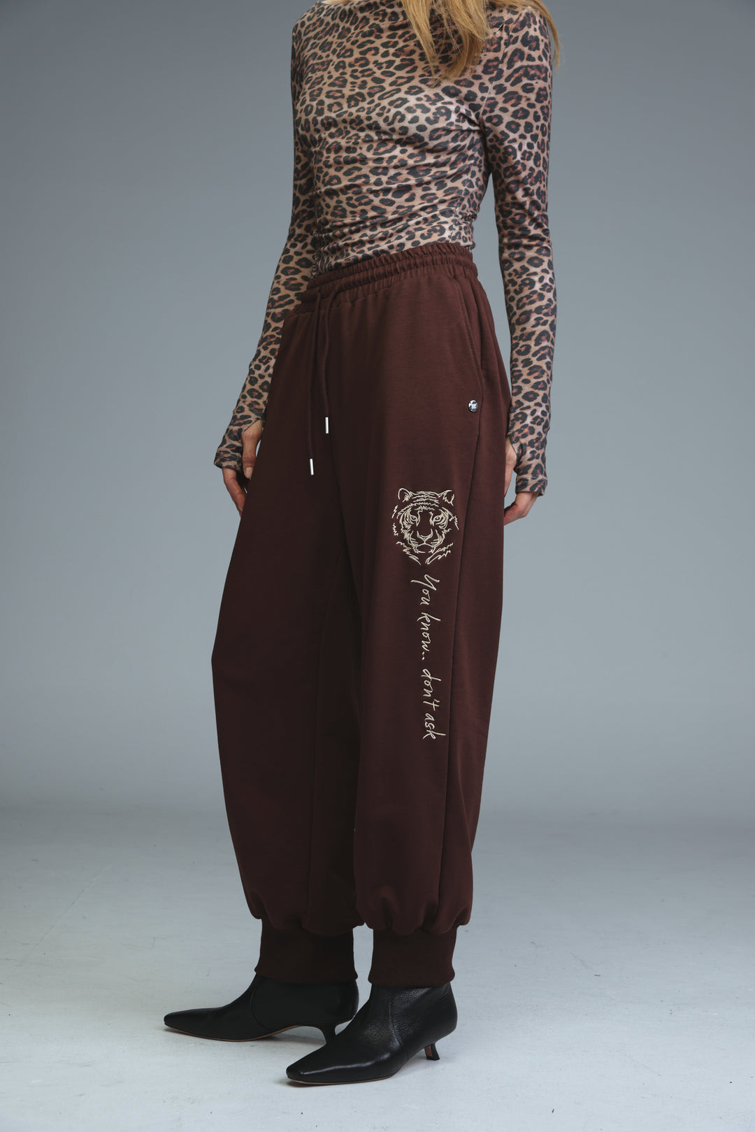 Brown tiger-themed jogger pants with drawstring waist and embroidered phrase shown from the front
