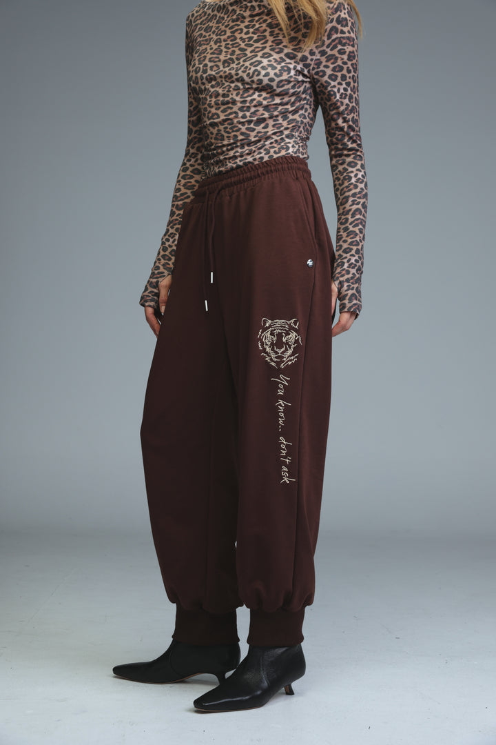 Brown tiger-themed joggers with drawstring waist and embroidered phrase shown from the front