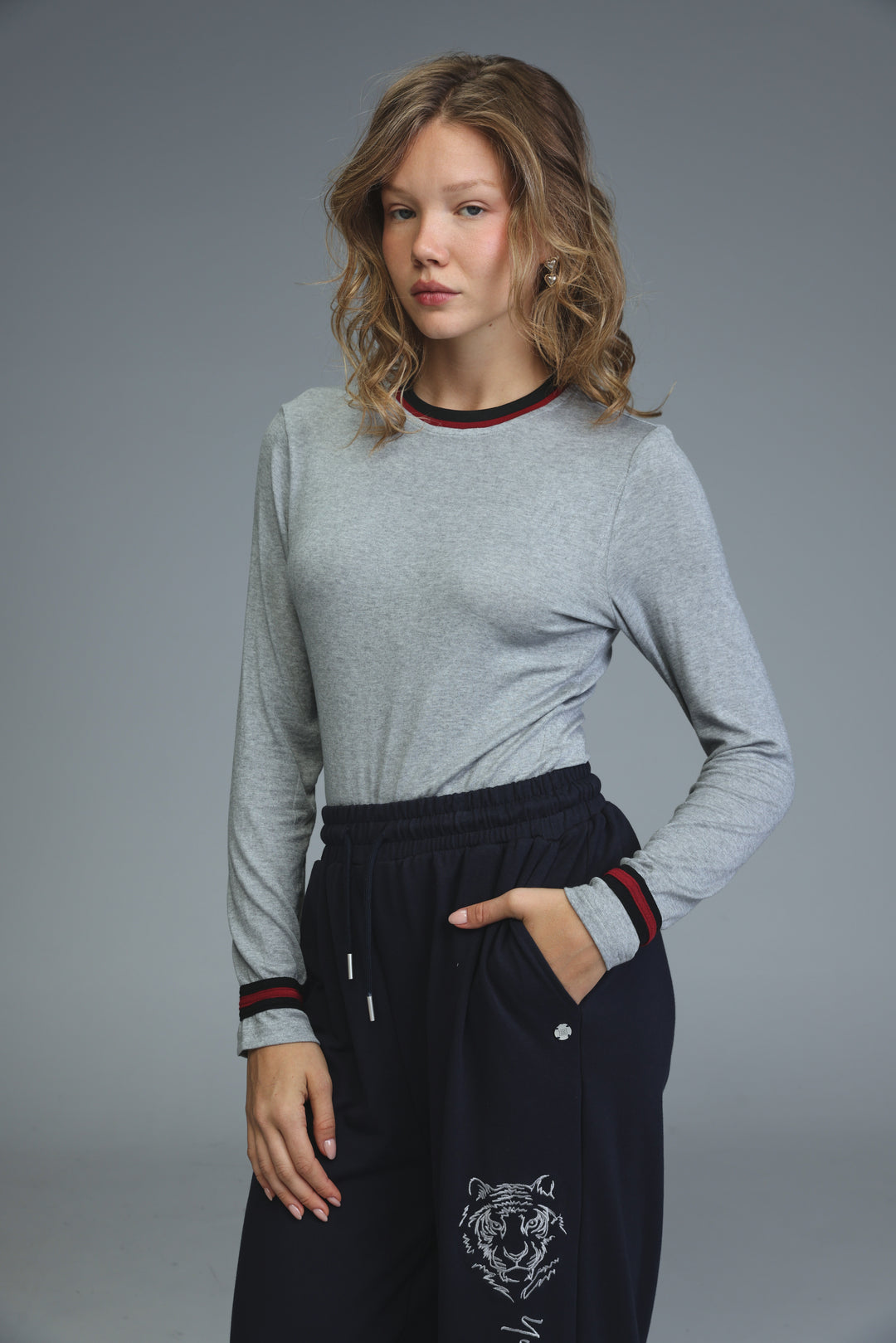 Gray long-sleeved bodysuit with black and red trim at neckline and cuffs paired with navy sweatpants with tiger embroidery