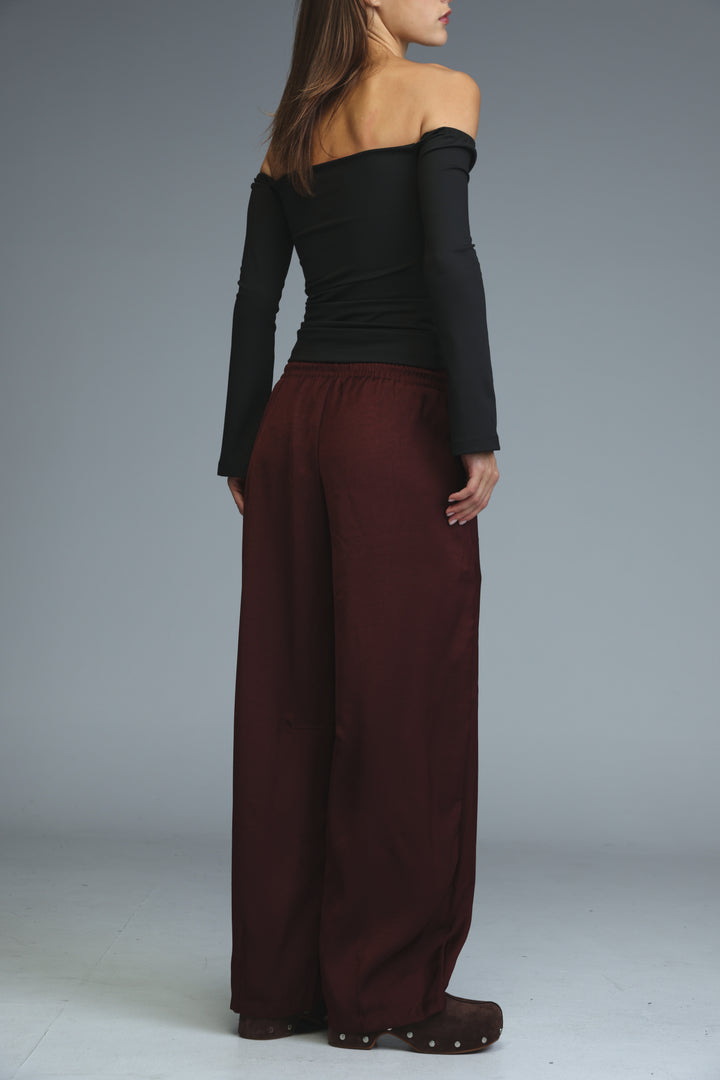The golden wine bottoms are wide-leg maroon trousers shown from the front paired with a black off-shoulder top
