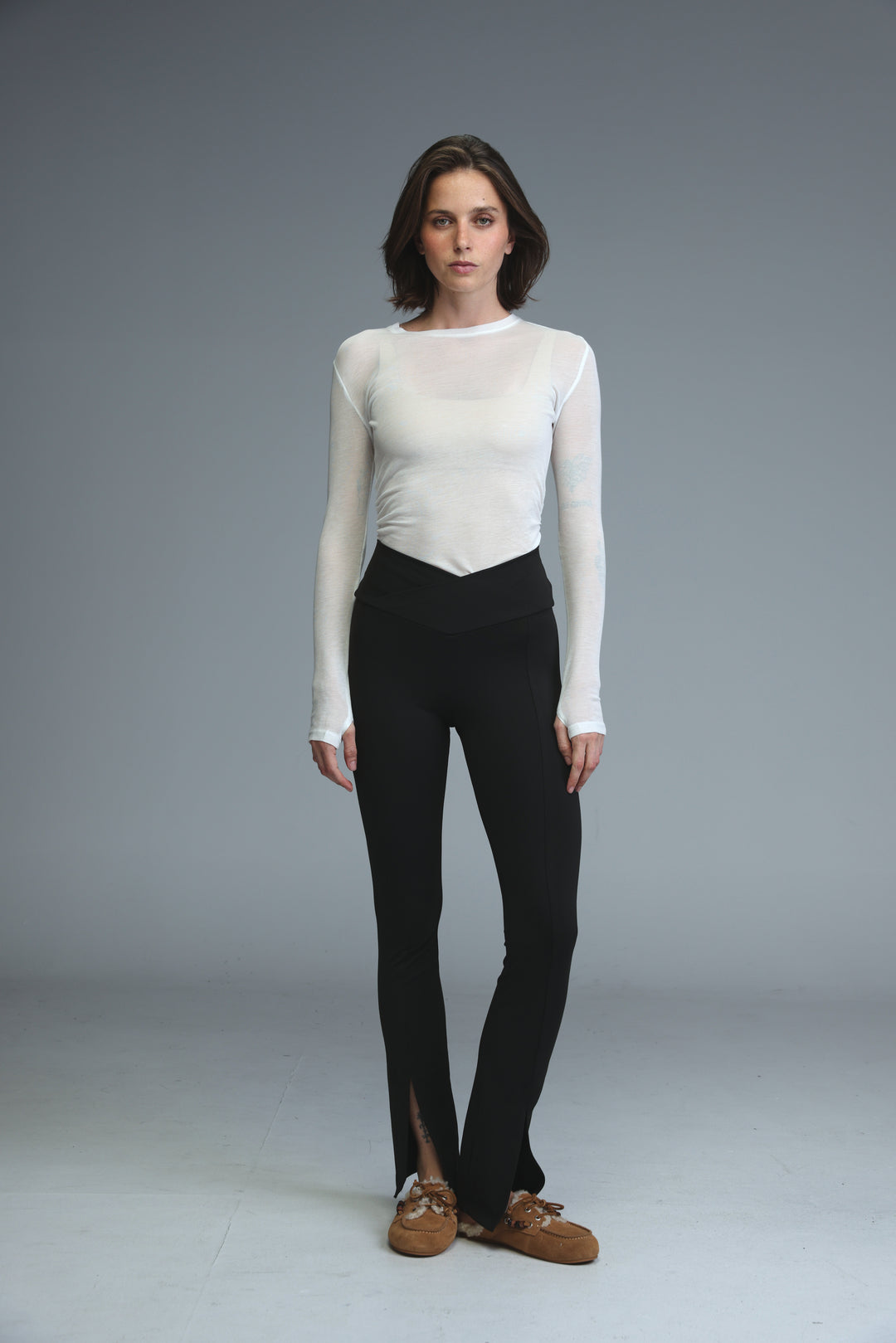 A front view of black high-waisted flared front slit black leggings paired with a white long-sleeved mesh top