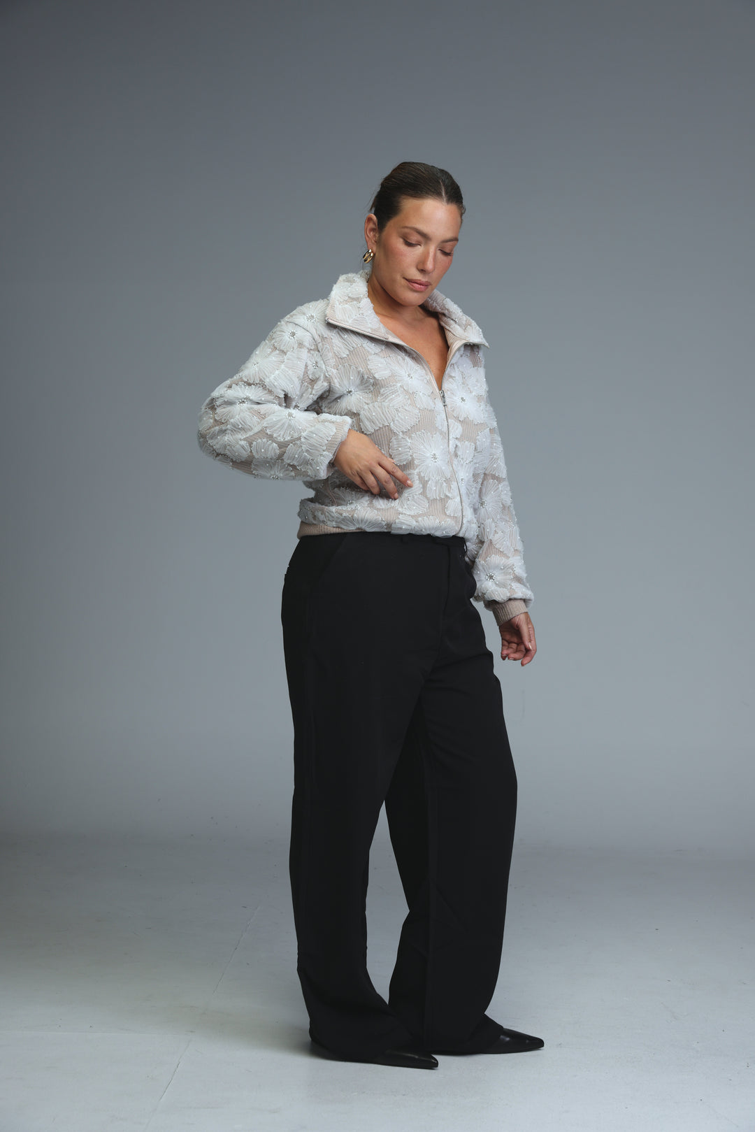 A woman wears mid rise tailored black bottoms viewed from the front paired with a white puffer jacket with floral pattern
