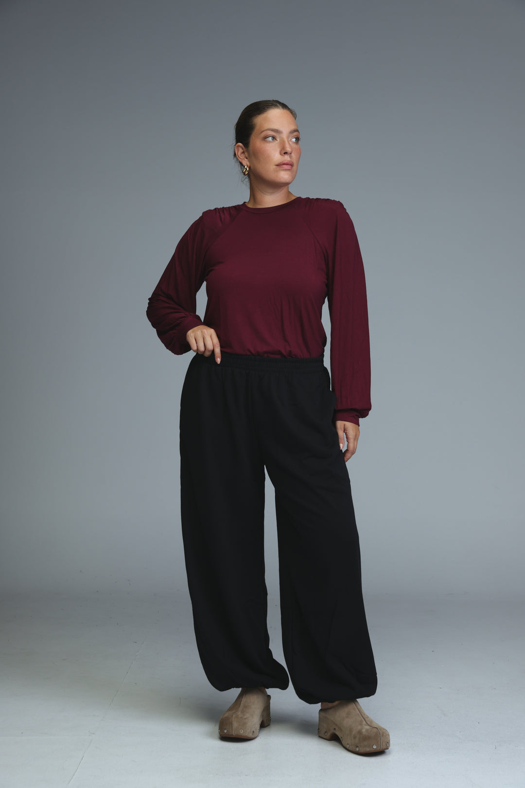 A woman wearing brown joggers shown from the front paired with a maroon long-sleeved top and tan suede clog shoes
