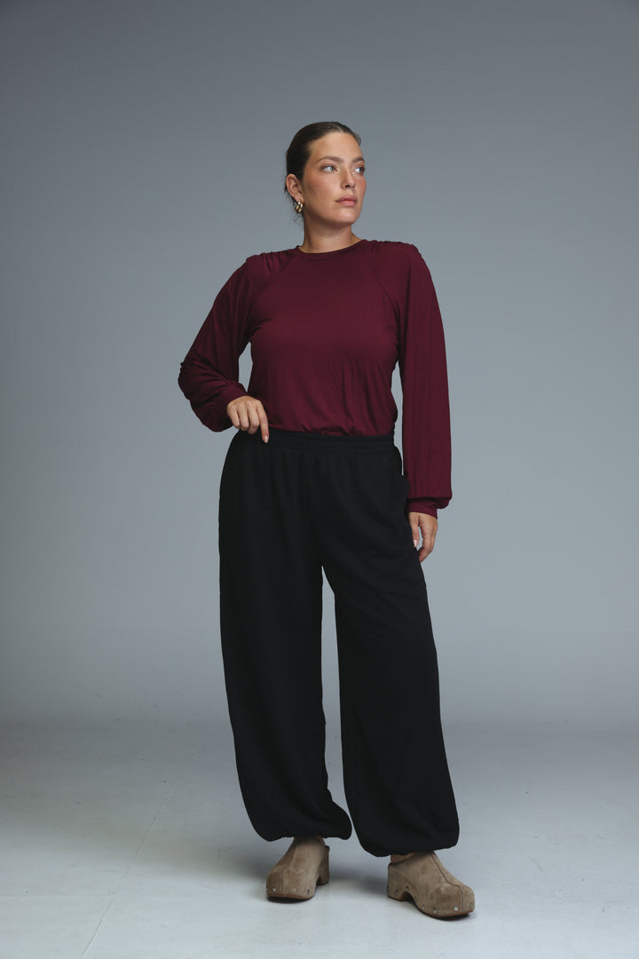A woman wearing brown joggers shown from the front paired with a maroon long-sleeved top and tan suede clog shoes