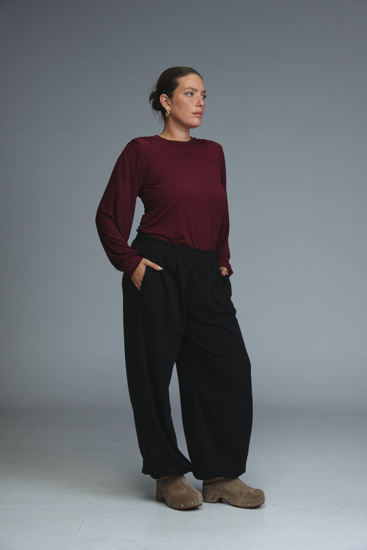 A woman wearing a maroon long-sleeved top and black wide-leg trousers stands next to blue joggers