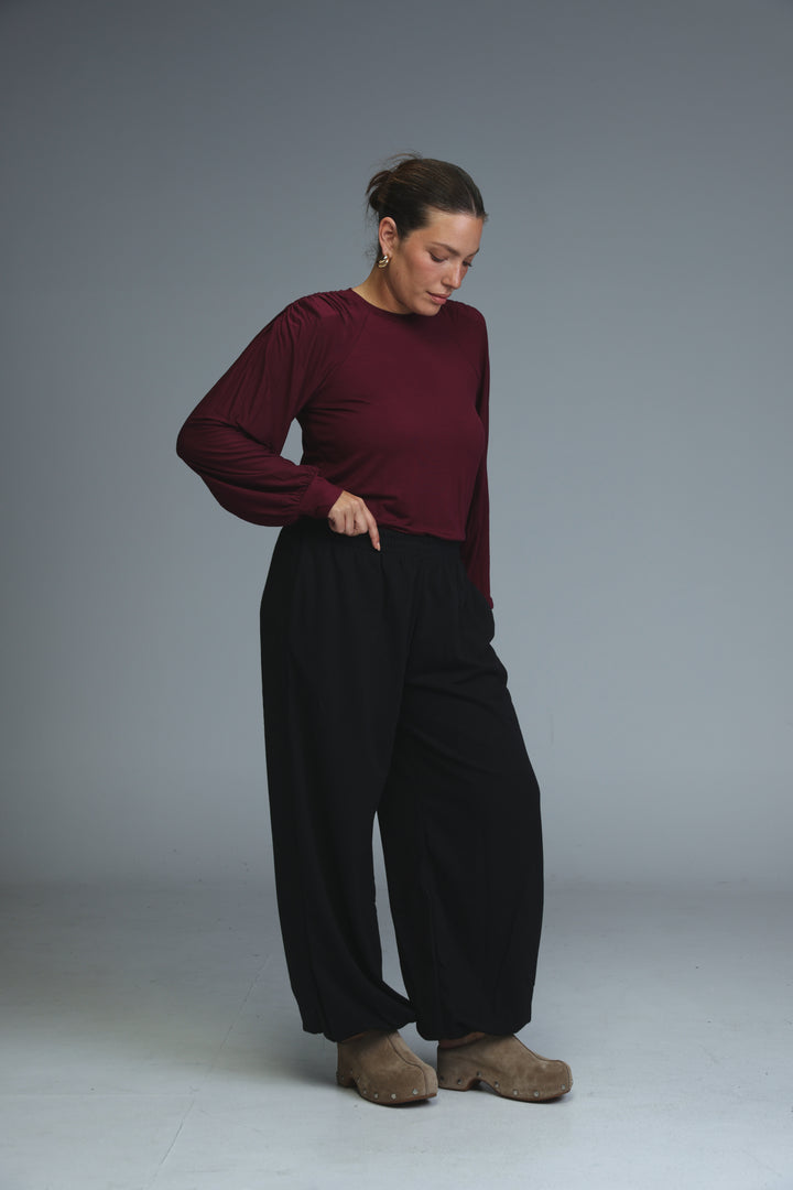 A woman wearing brown joggers paired with a maroon long-sleeved top with puffed sleeves and black wide-leg trousers