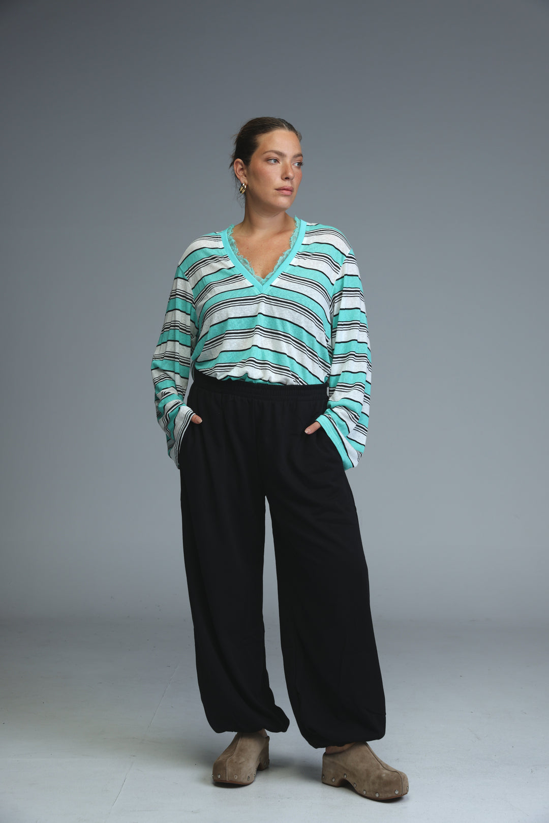 A front view of a glow grey striped shirt with a v-neck long-sleeved design worn with black pants