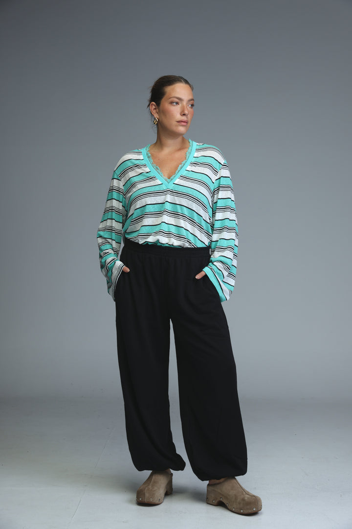 A front view of a glow grey striped shirt with a v-neck long-sleeved design worn with black pants